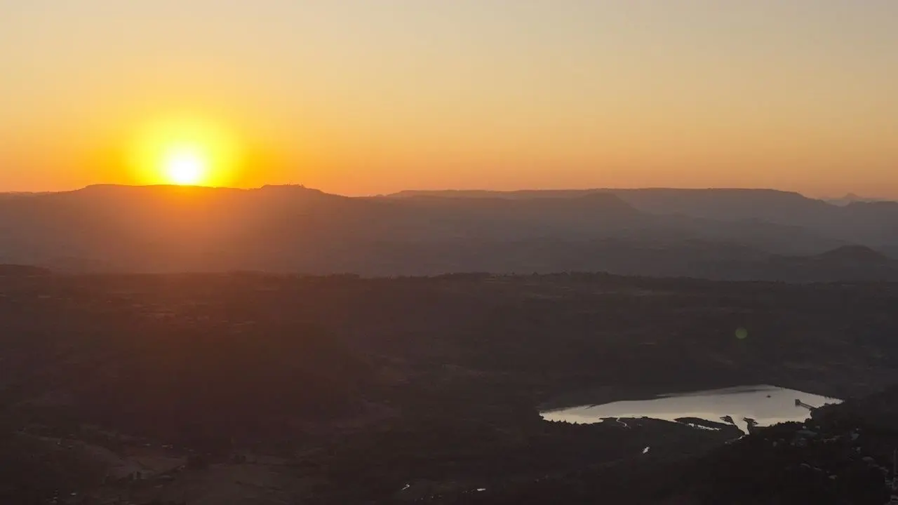 Sun setting over distant hills with a lake in the valley below