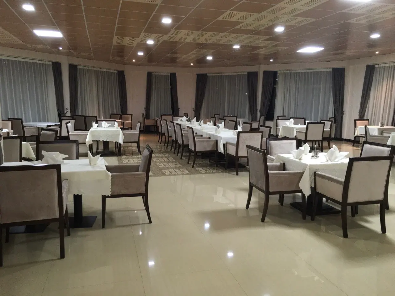 Large restaurant hall with white-clothed tables under a ceiling of spotlights