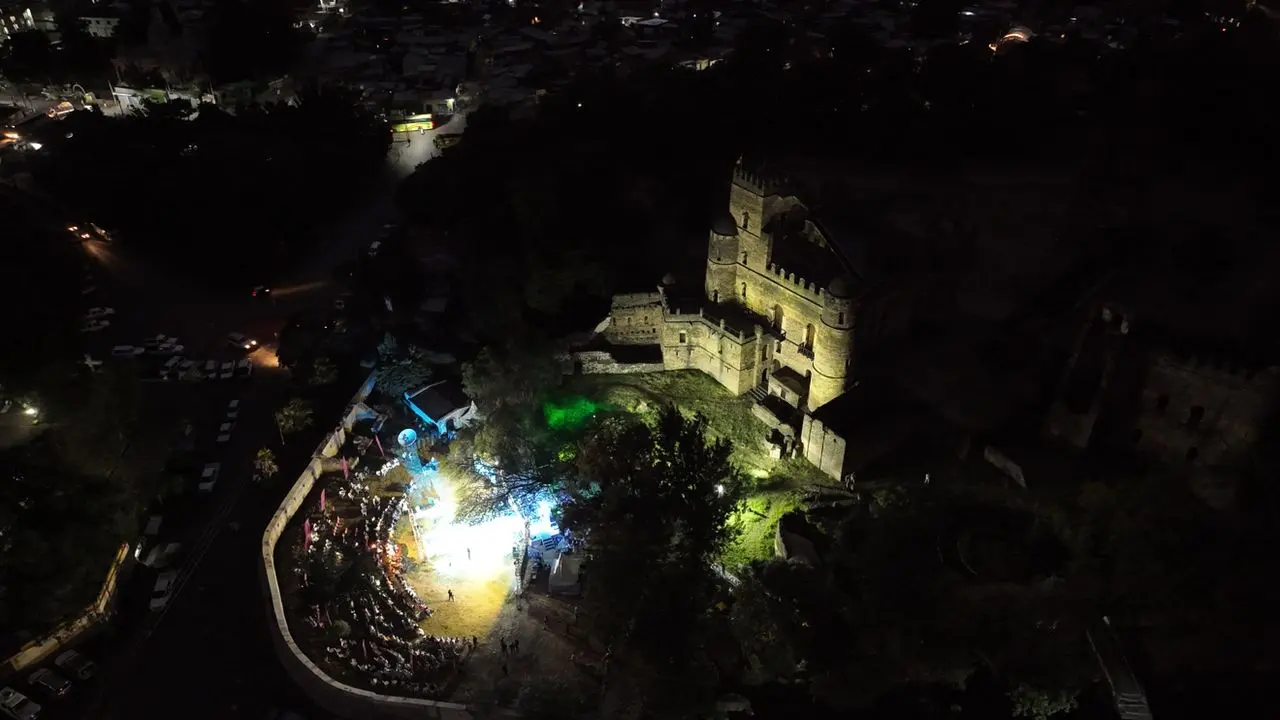 Night aerial view of a floodlit stone castle and a crowd at a lit outdoor event