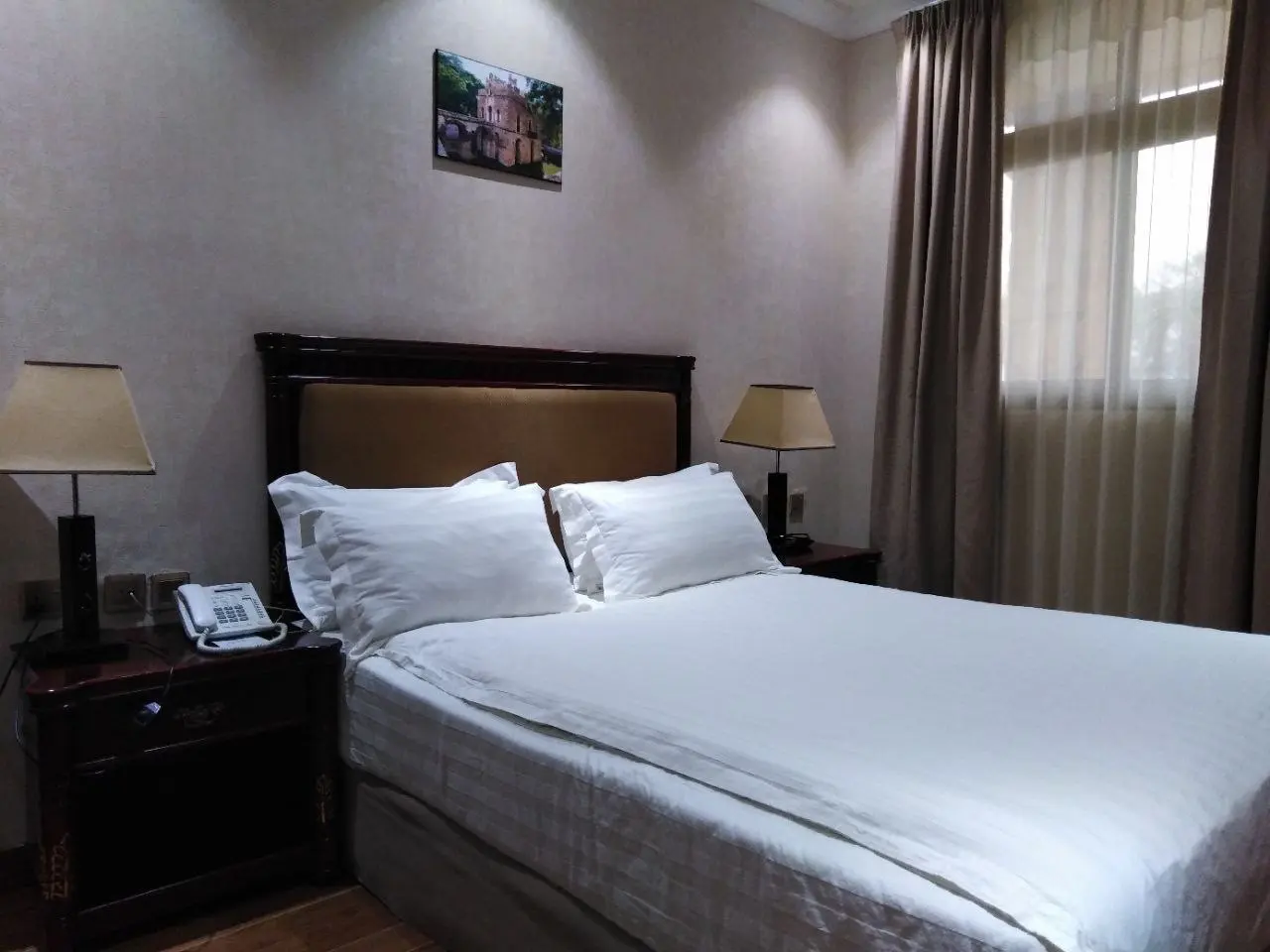 Standard room double bed with a framed picture above and a bedside phone