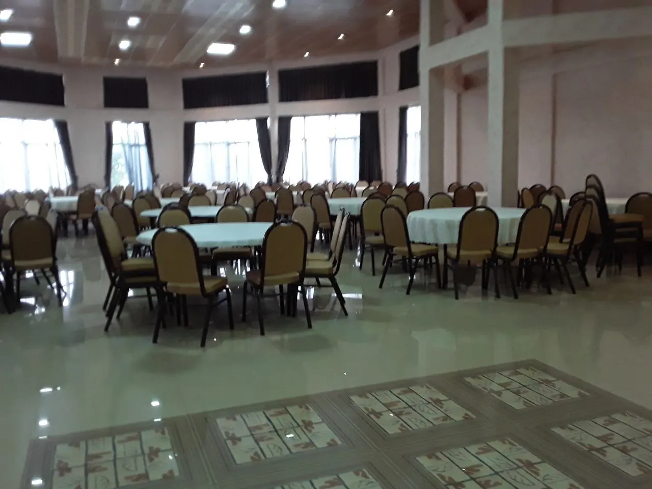 Conference hall with round tables and gold chairs beside tall windows