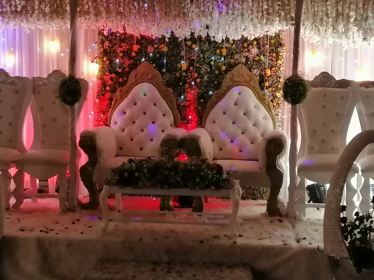 Decorated stage with two ornate white and gold armchairs and flowers