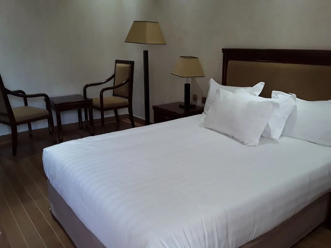 Close view of a standard room double bed with two armchairs and a lamp